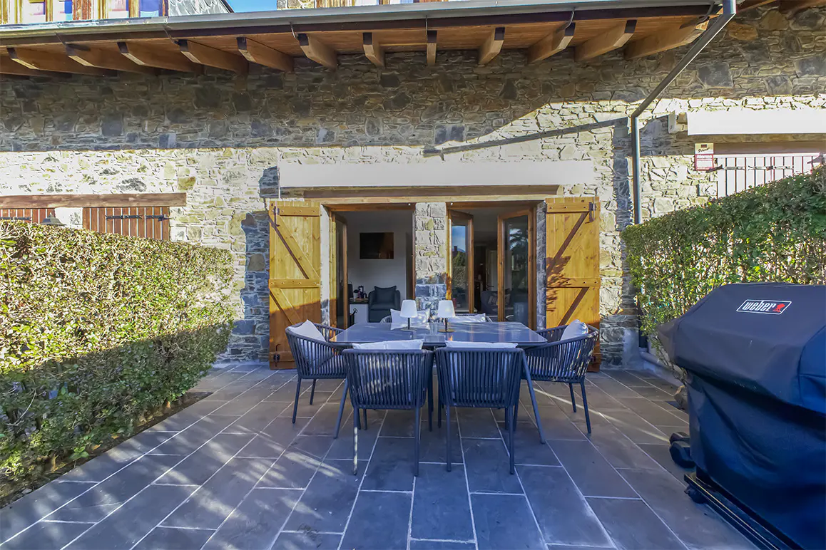 Outdoor patio with stone walls, wooden shutters, dining table with chairs, and a covered grill.