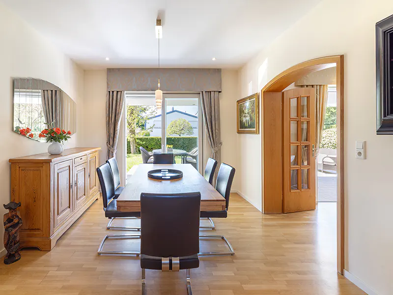 Bright dining room with wood floors, table, and chairs. Sliding glass doors lead to a green backyard. A wooden cabinet sits against the wall.