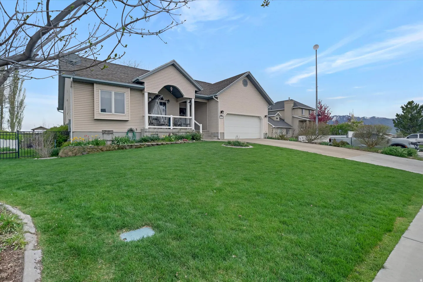 Tan two-story house with a green lawn, a porch with a swing, and a driveway leading to a garage.