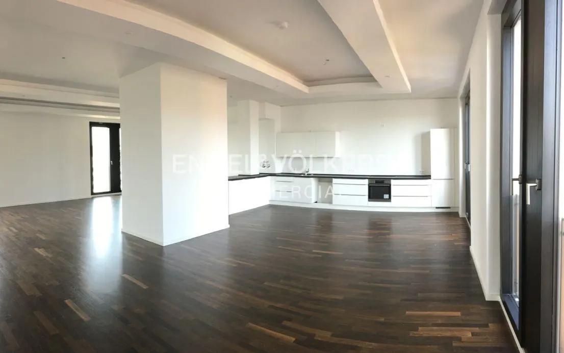 A panoramic view of a modern apartment with dark wood floors, white walls, and a white kitchen. Black framed windows are on either side.