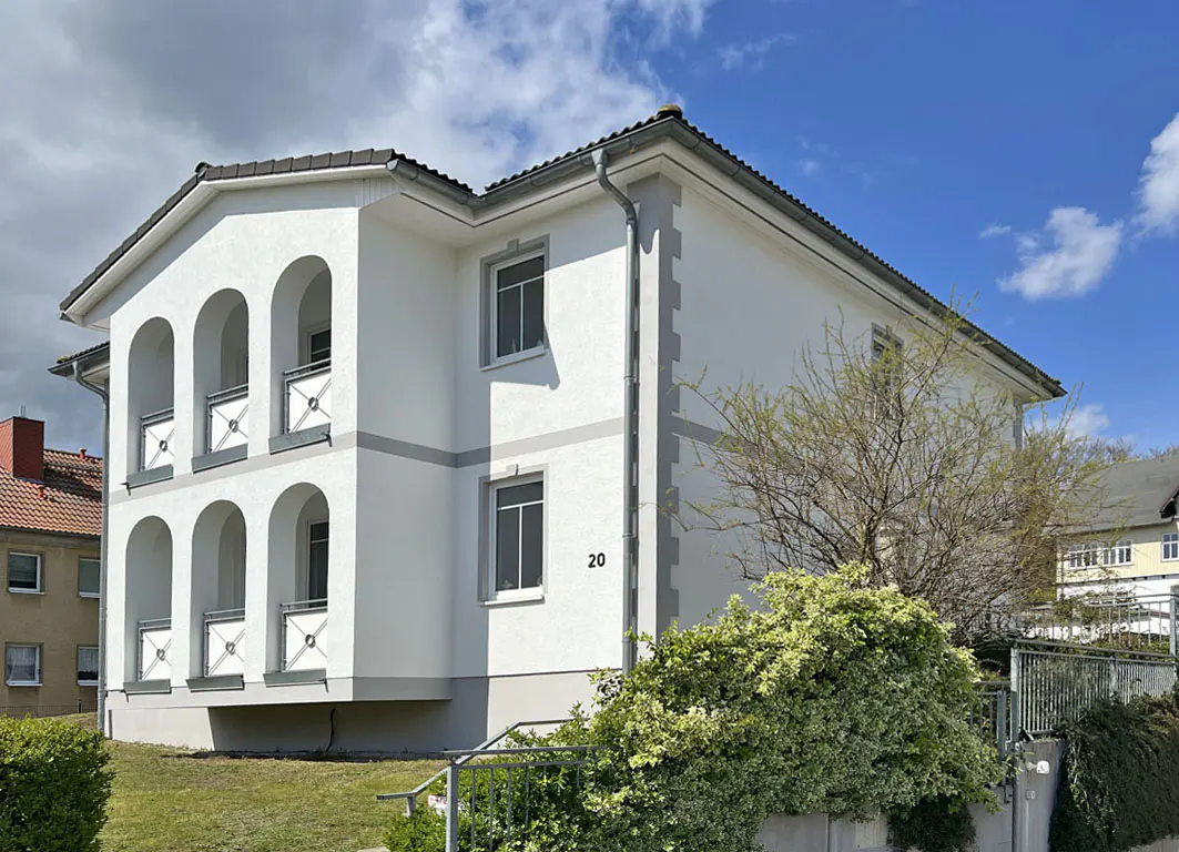 Two-story white house with arched balconies, gray trim, and the number 20 on the side, set against a blue sky.