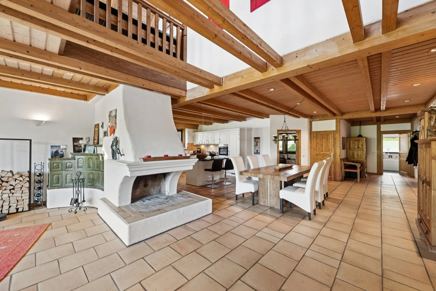Open-concept living space with a white fireplace, wood beams, tile floors, and a dining table with white chairs.