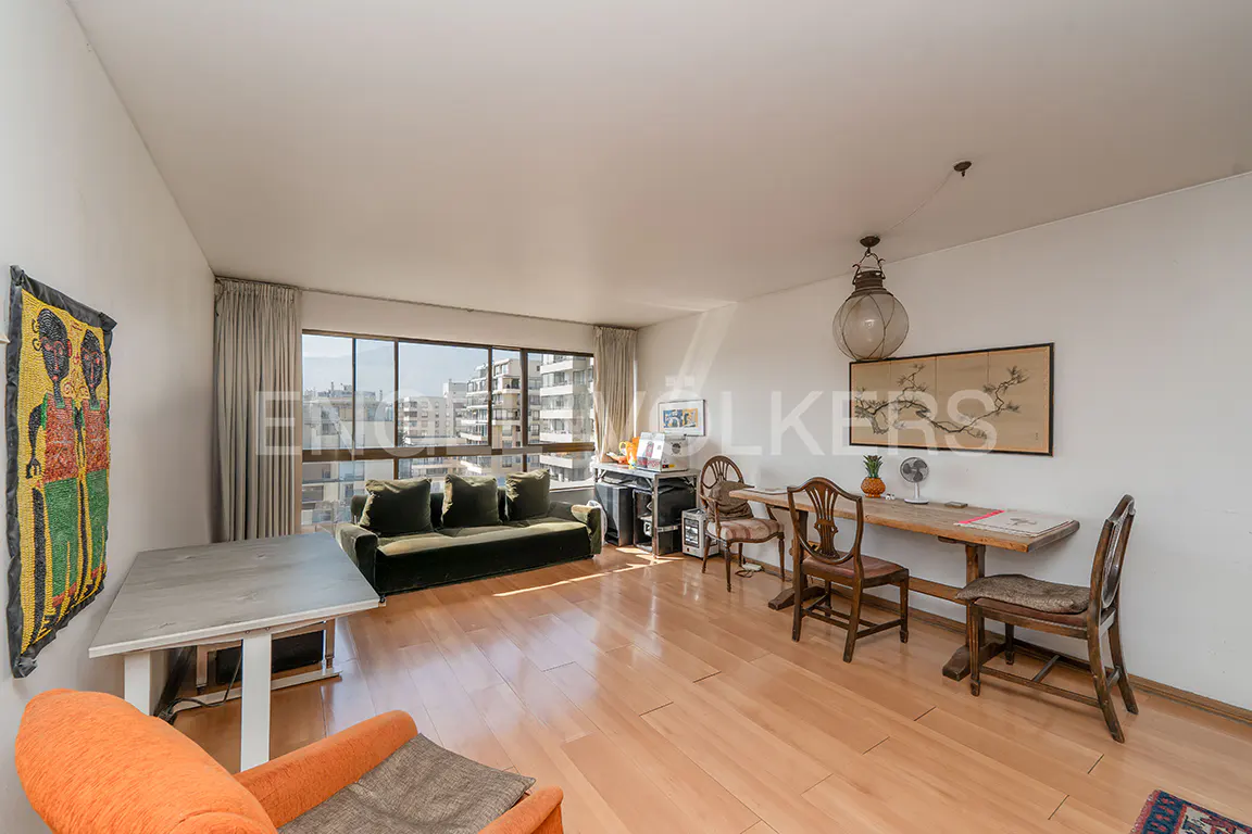Bright living room with light wood floors, a green sofa, a dining table with chairs, and an orange armchair.