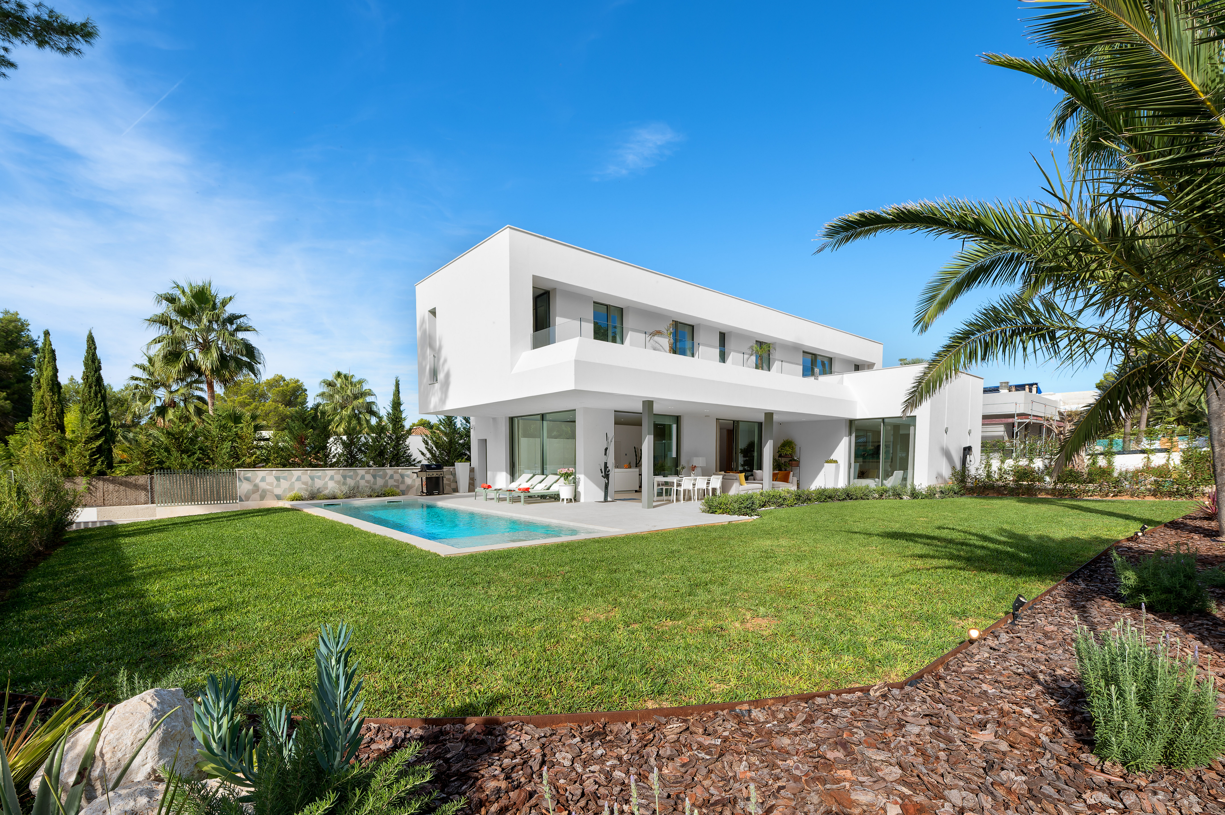 Modern white two-story villa with a swimming pool, lush green lawn, and palm trees under a clear blue sky. [AI-generated text]