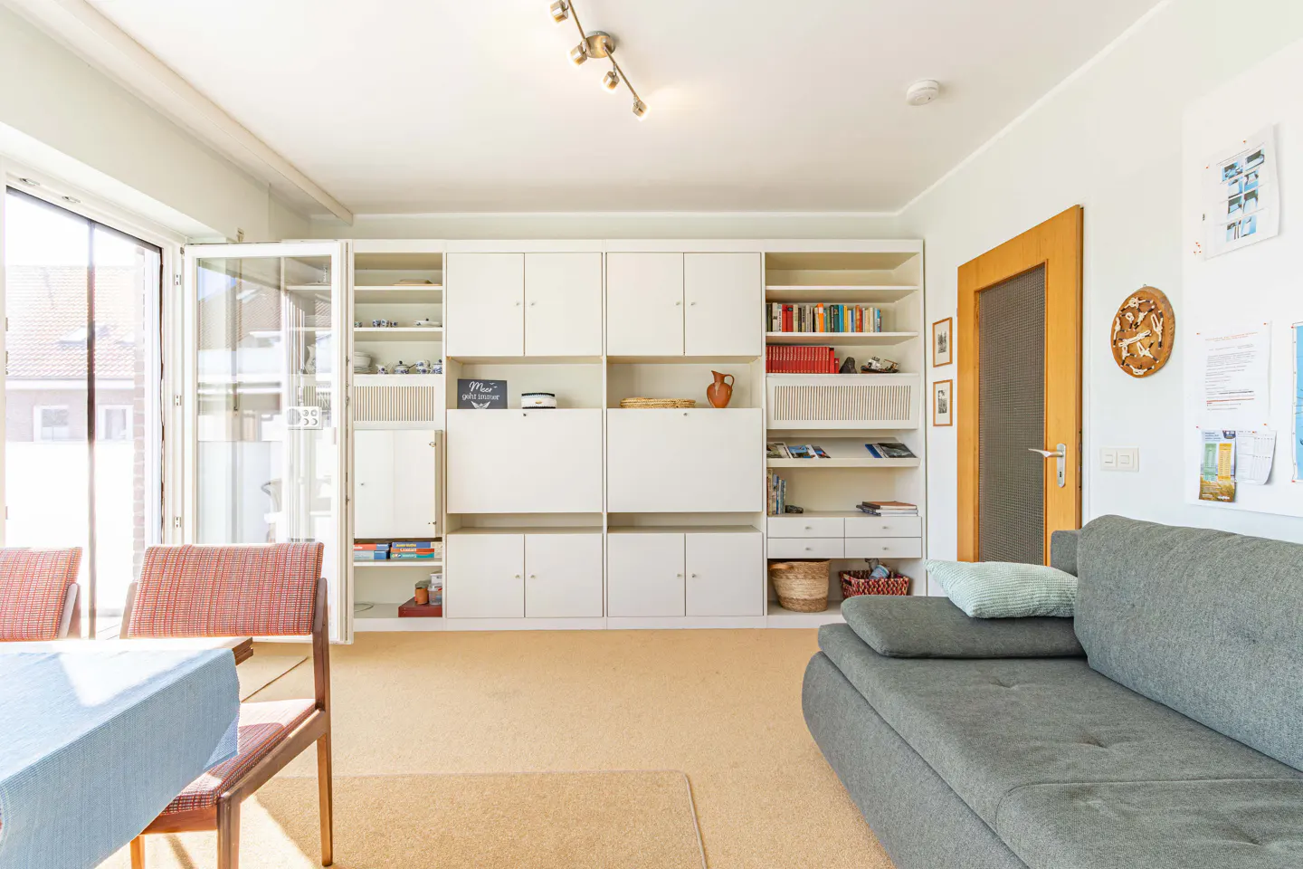 Living room with a gray sofa, a dining table with chairs, and a large white built-in bookcase.