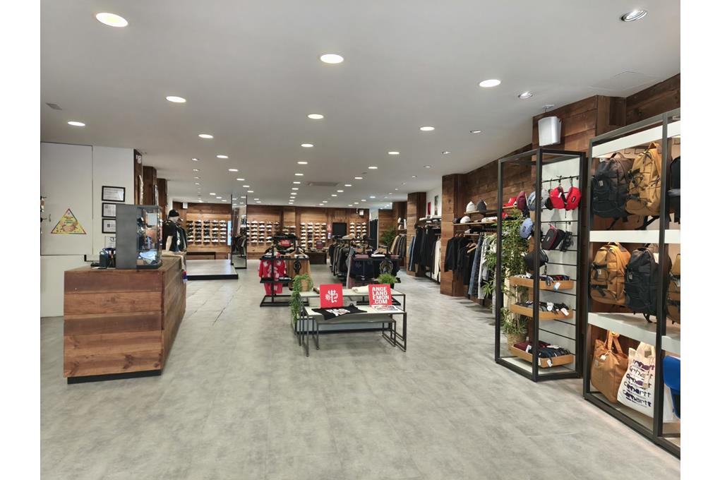 Interior of a modern clothing store with wooden walls, concrete floors, clothing racks, and shelves displaying backpacks. [AI-generated text]