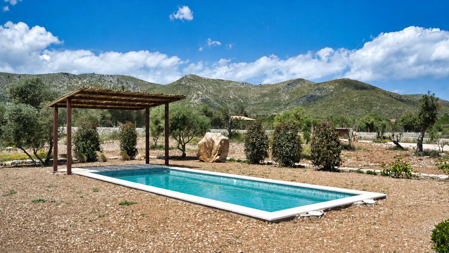 A rectangular pool with turquoise water and a pergola, set against a mountain backdrop.