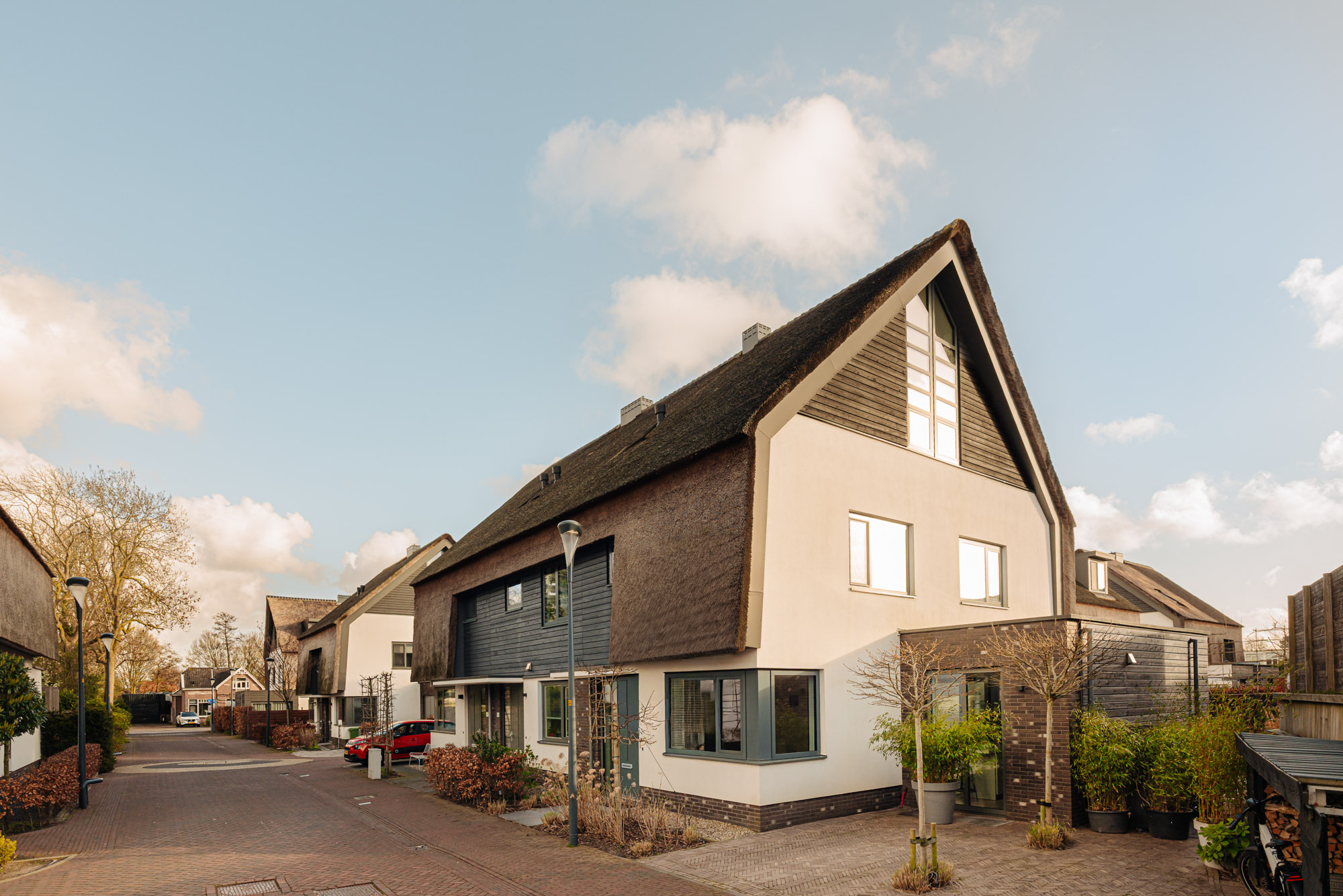 Street view of a modern house with a thatched roof and white walls under a blue sky.
