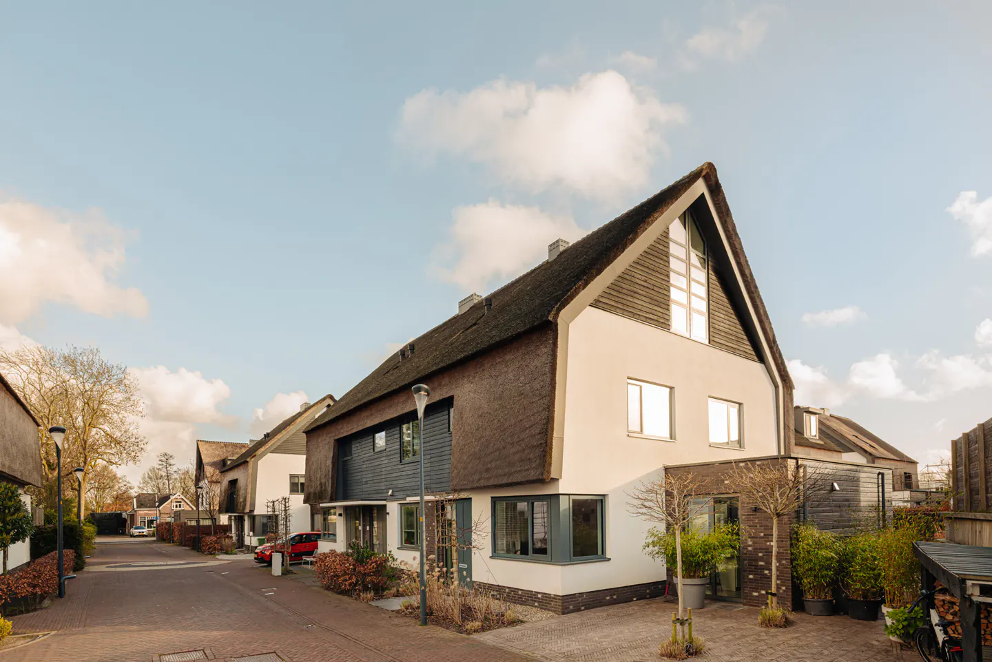 Street view of a modern house with a thatched roof and white walls under a blue sky.