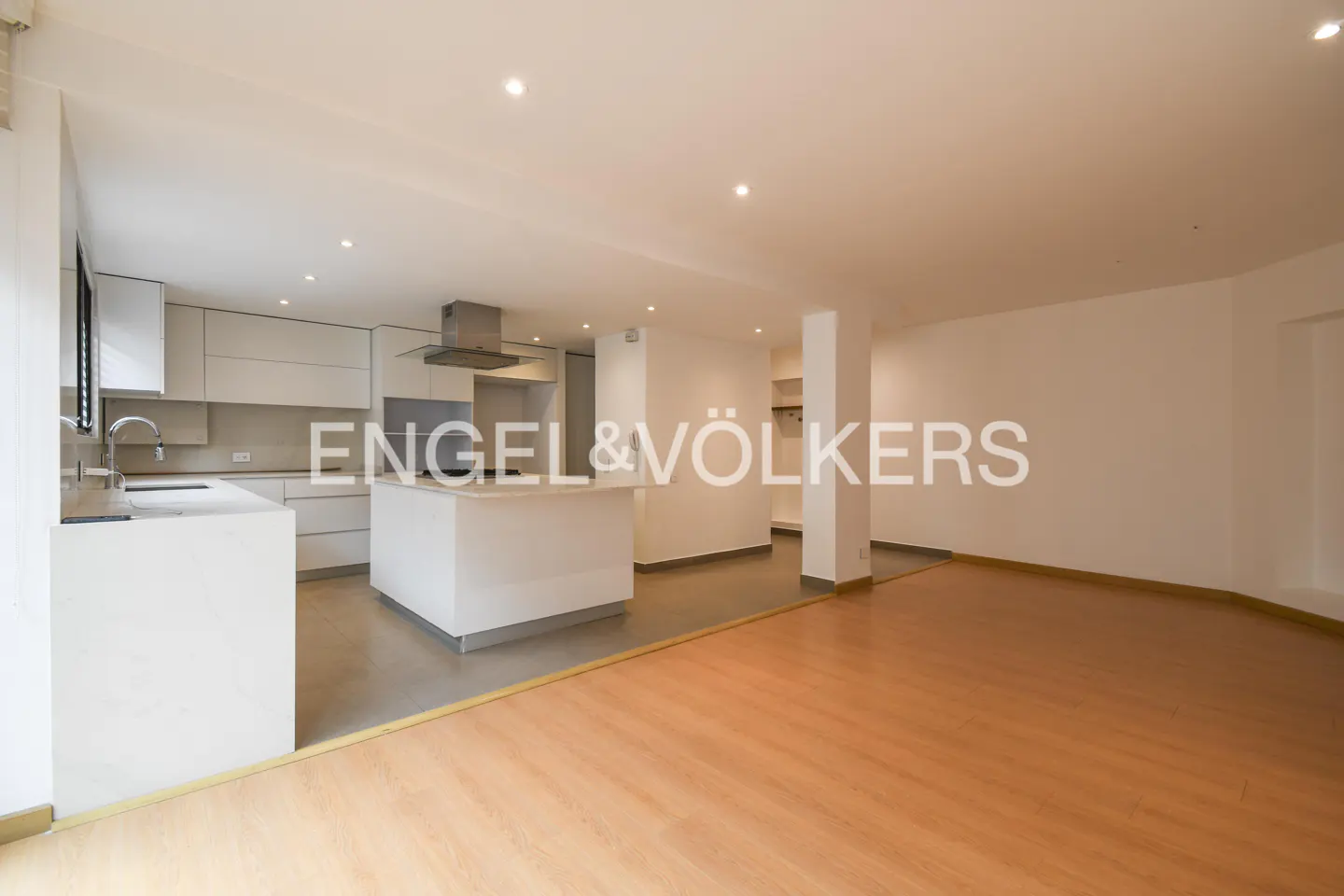 Bright, open-concept kitchen and living area with white cabinets, island, stainless steel hood, and light wood floors.