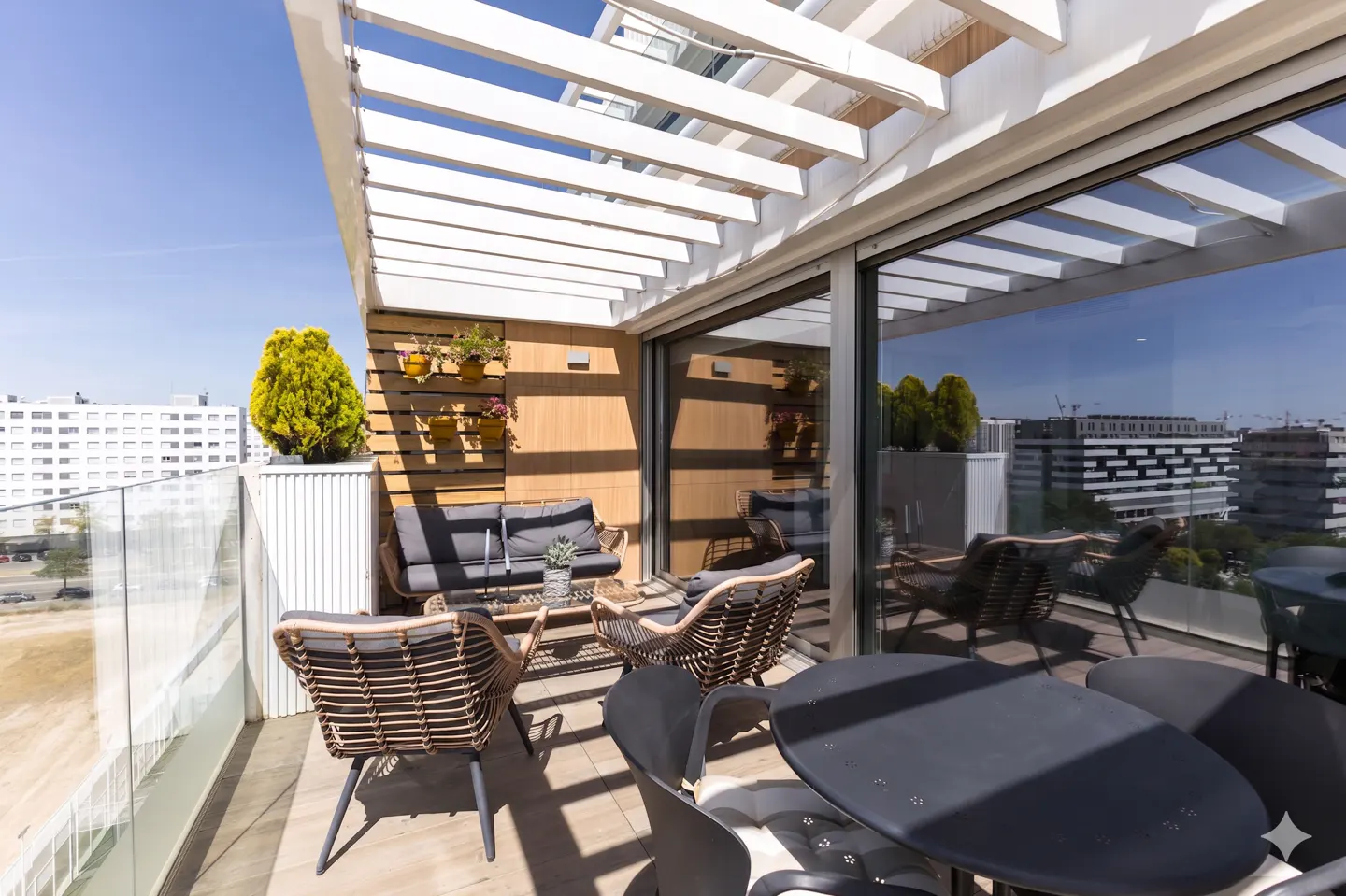 Modern balcony with a white pergola, wicker lounge furniture, a dining table, and a vertical garden on a wood-paneled wall.