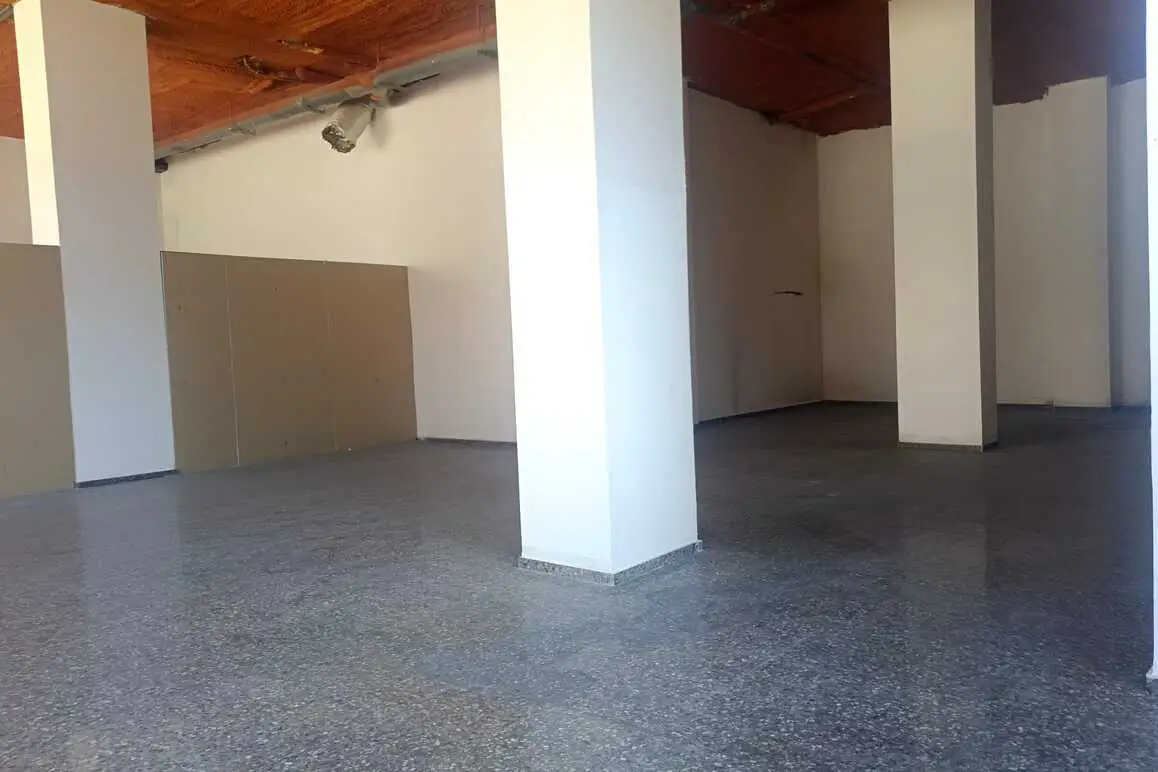 Empty commercial space with white walls, gray floors, and white support columns. The ceiling is exposed with orange insulation.