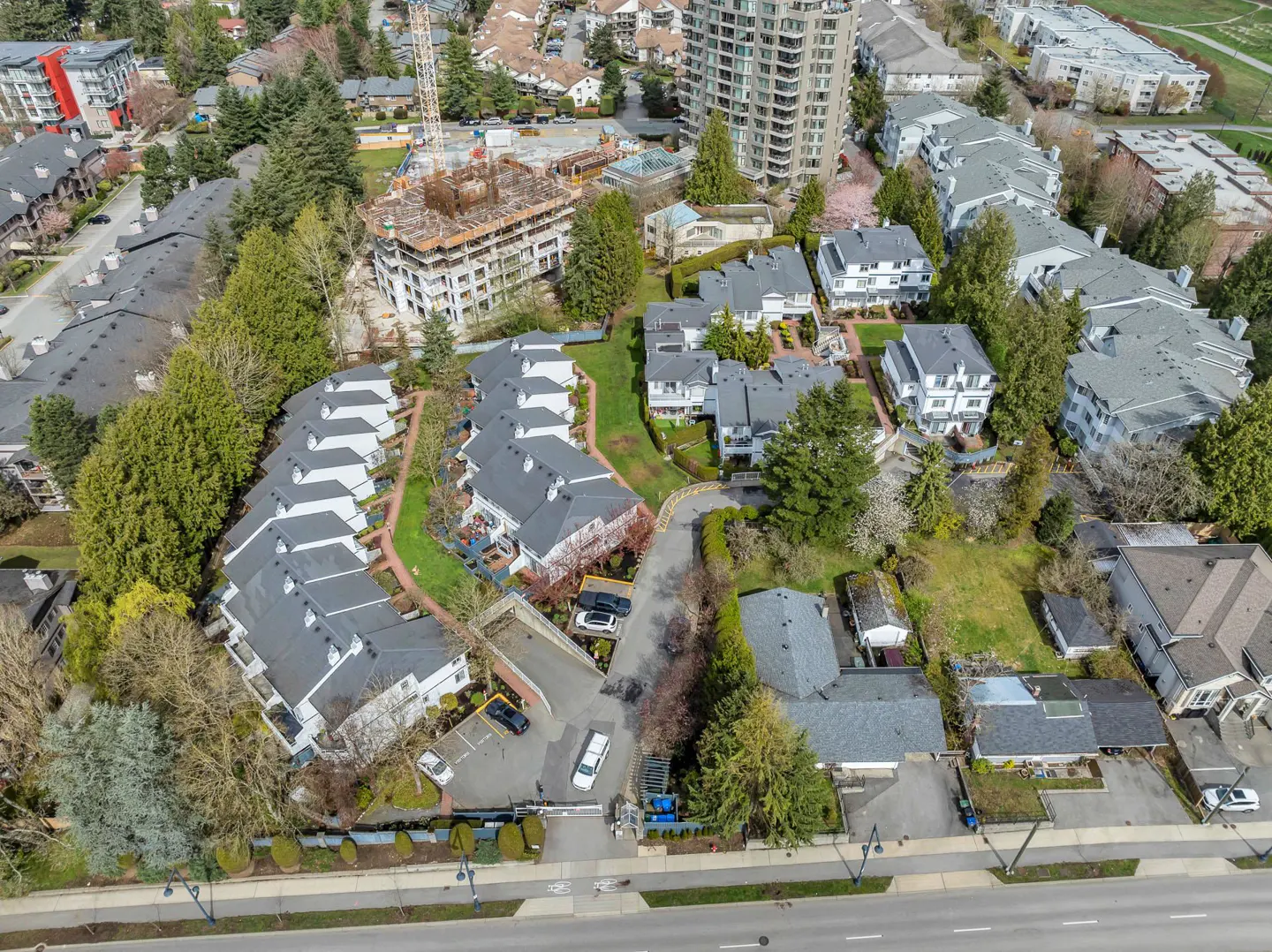 Aerial view of a residential area with townhouses, trees, and a construction site in the background.