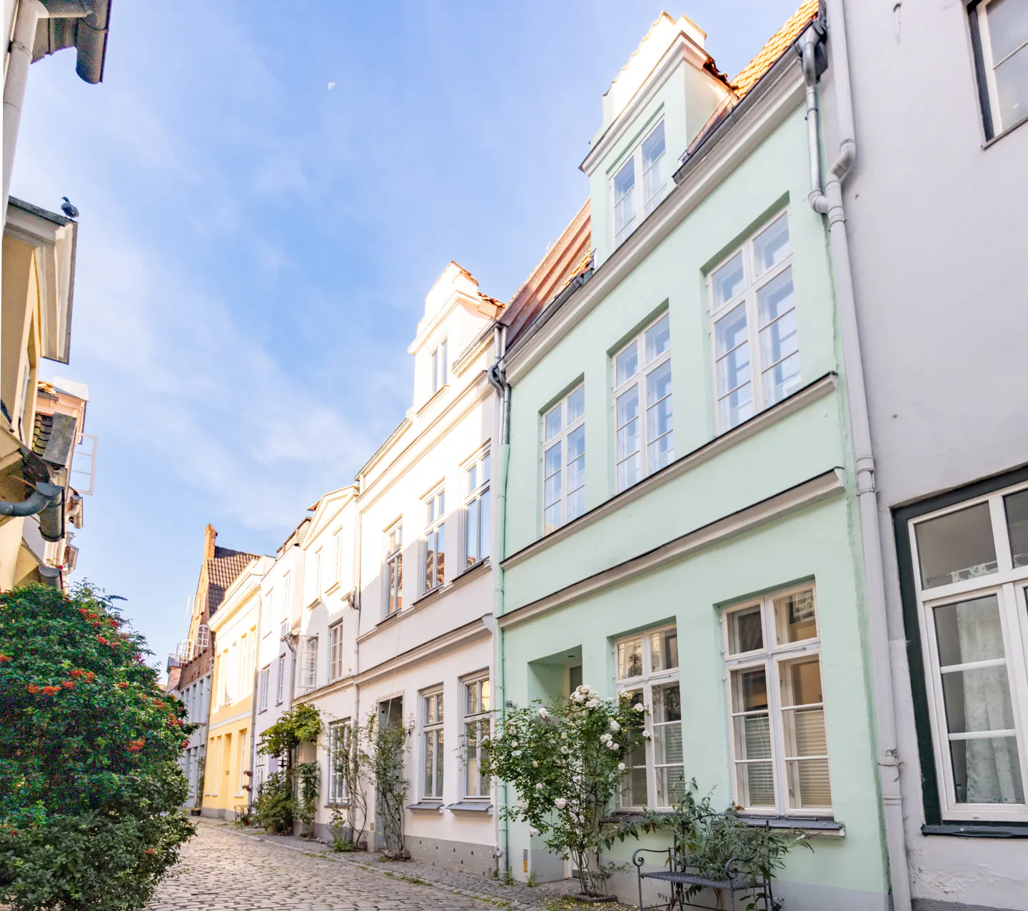 Cobblestone street lined with colorful townhouses in pastel shades of green, white, and yellow under a bright blue sky.