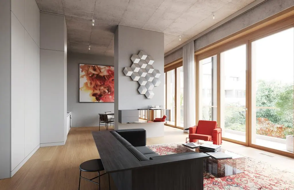 Bright, modern living room with wood floors, large windows, and a black sectional sofa. A red armchair sits on a patterned rug. Abstract art adorns the walls.