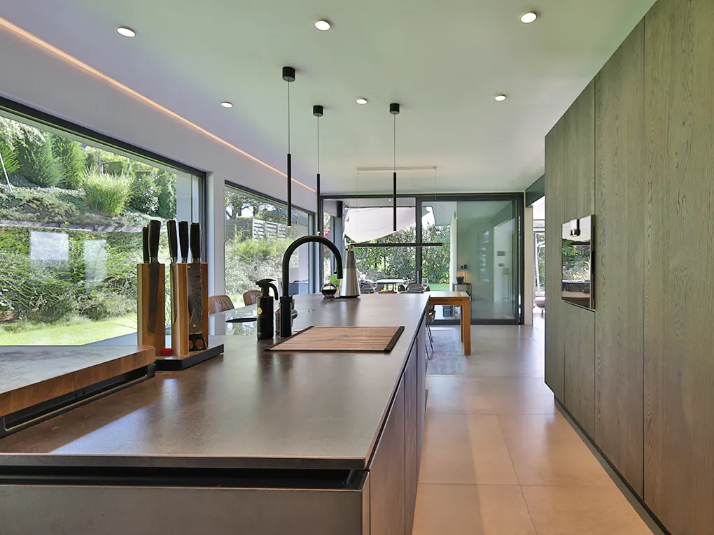 Modern kitchen with a large island, black faucet, and knife block. A large window overlooks a green lawn.