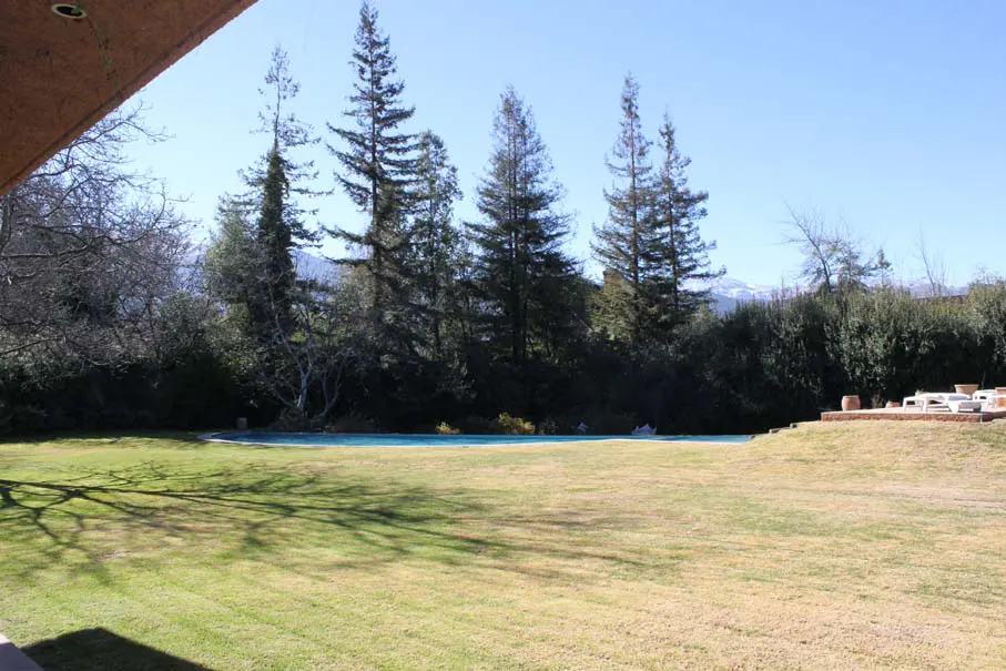 A large green lawn with a pool, trees, and mountains in the background.