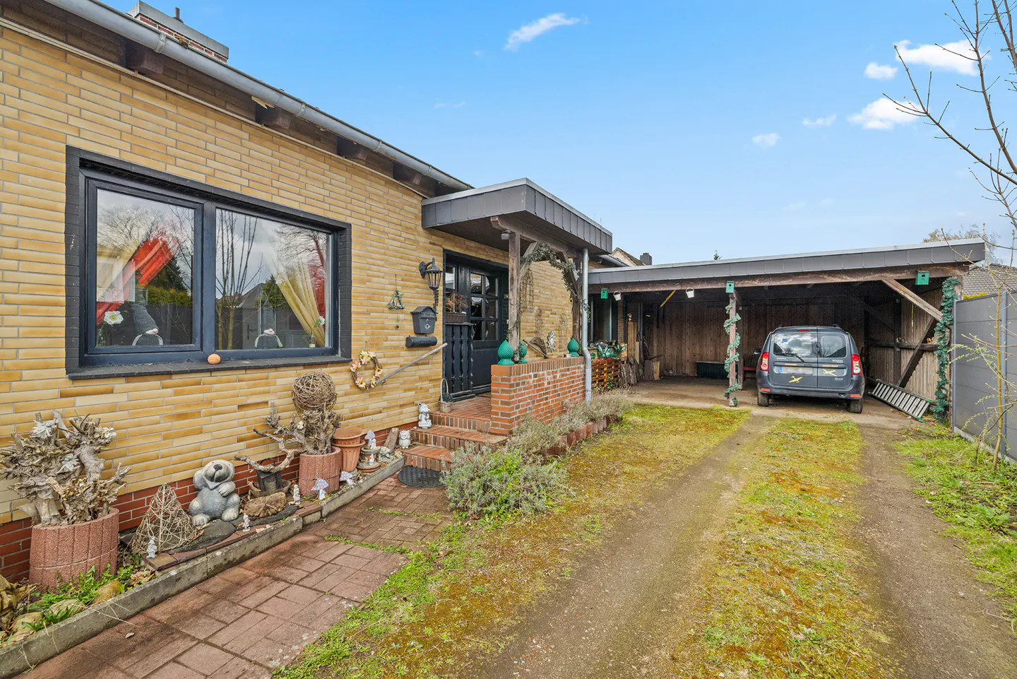 Exterior view of a one-story yellow brick house with a carport and a black van parked inside.