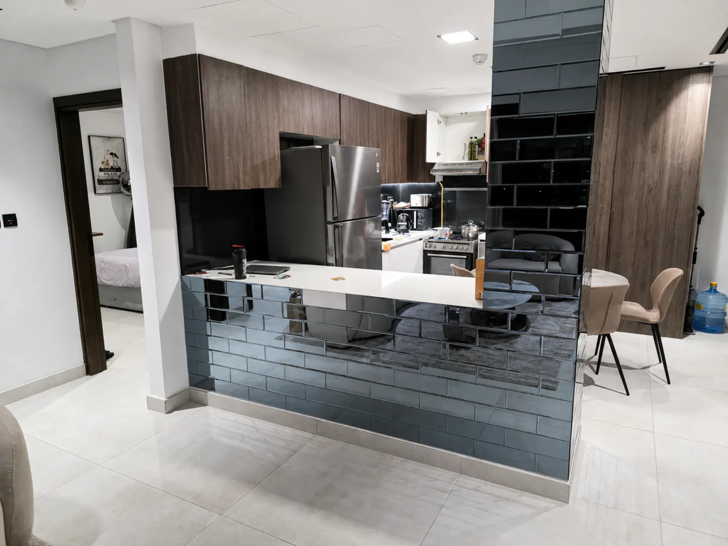 A modern apartment kitchen with dark wood cabinets, stainless steel appliances, and a mirrored brick-style breakfast bar.