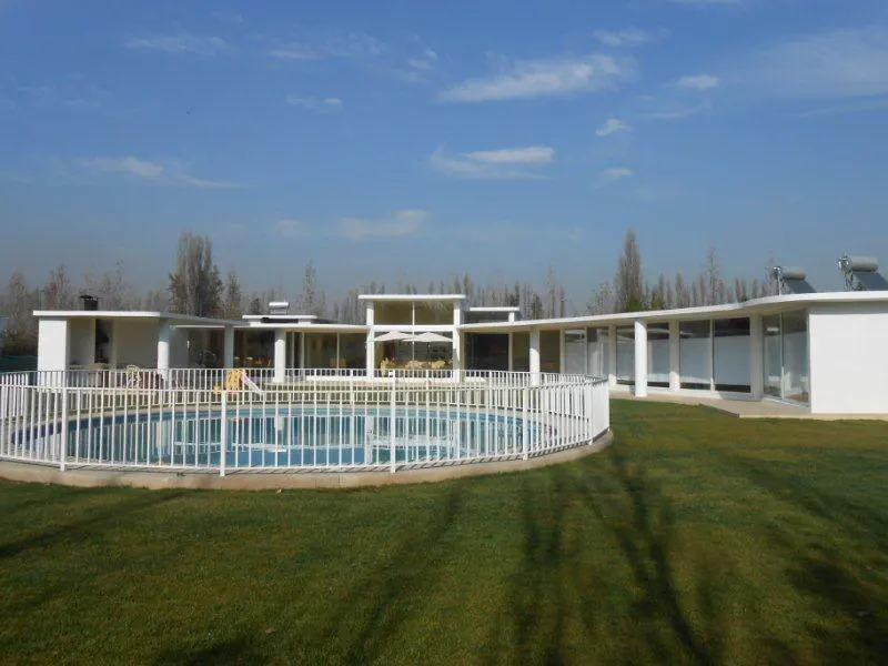 A modern white house with a pool, surrounded by green grass and a white fence, under a blue sky.