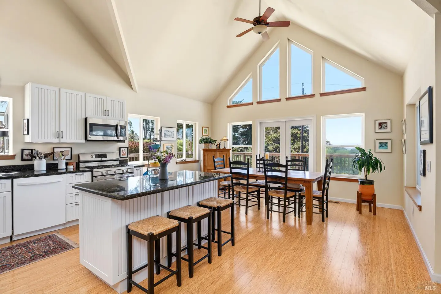 Bright, open kitchen with white cabinets, black granite counters, and a large island with seating. Dining table near windows with a view.