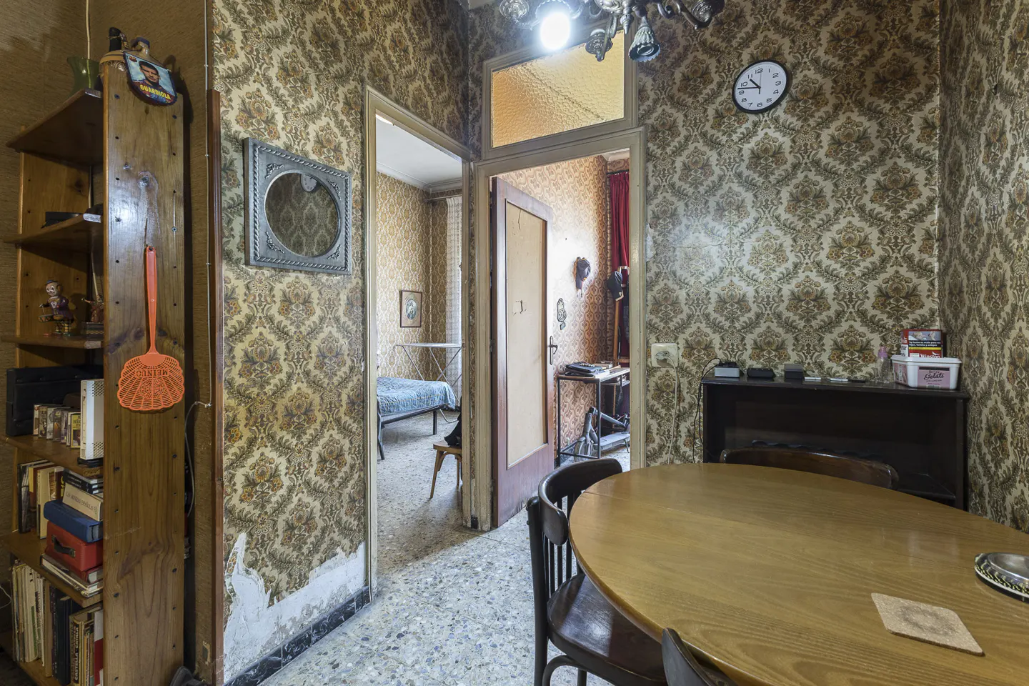 A vintage-style room with patterned wallpaper, a wooden table, and doorways leading to other rooms.