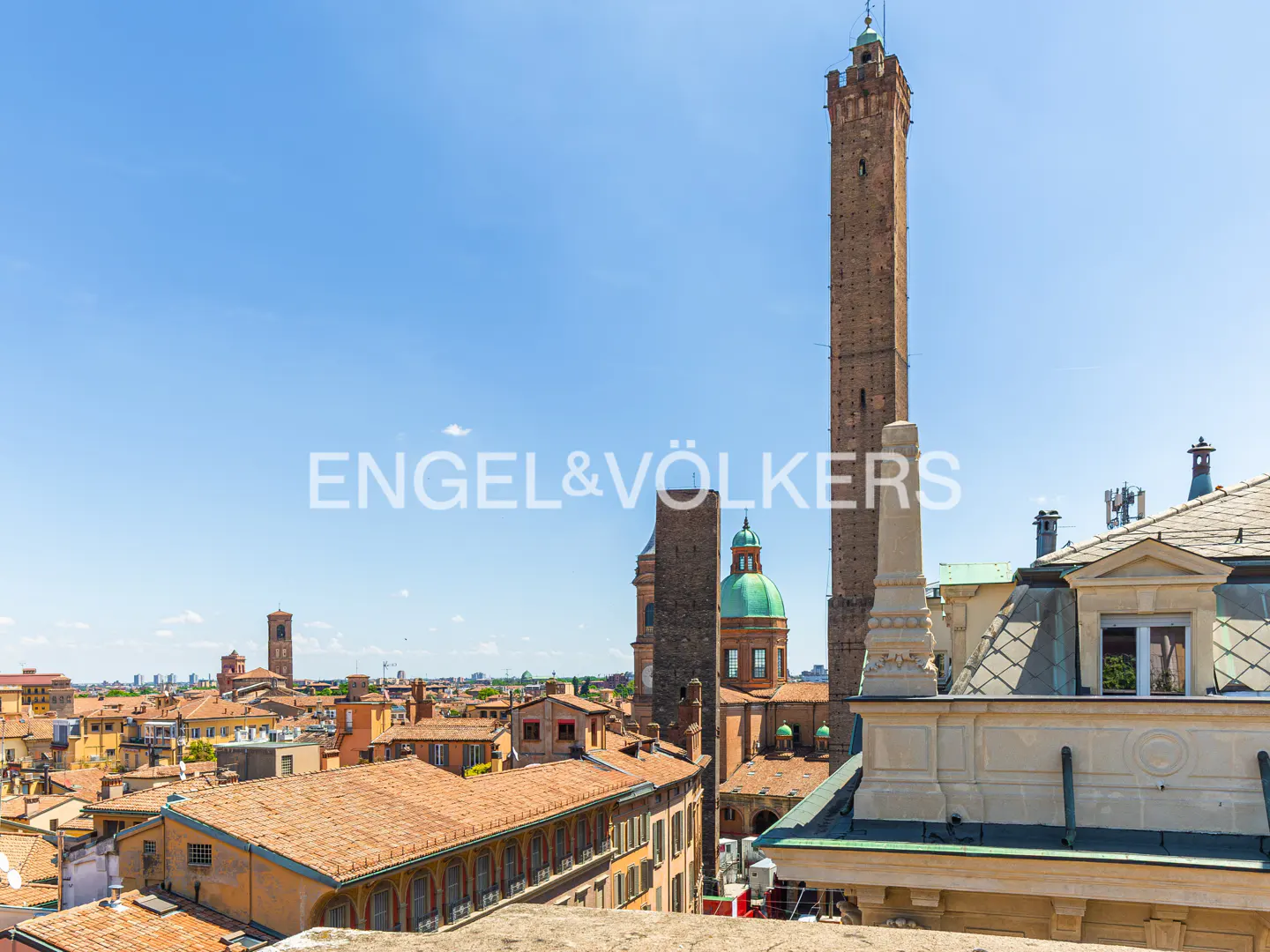 Bologna, Italy cityscape with terracotta rooftops, towers, and a green-domed church under a clear blue sky.