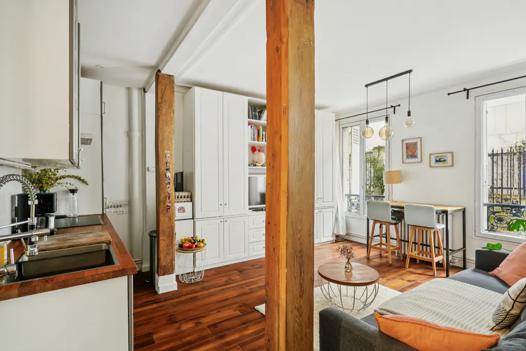 Open-plan apartment with a kitchen, wooden floors, a rustic support beam, white cabinetry, and a cozy living area.