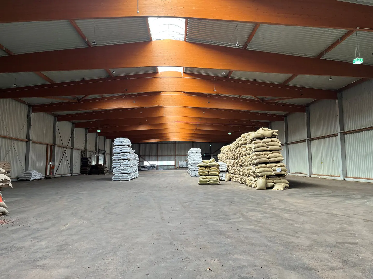 A large warehouse interior with stacks of burlap sacks under a wooden beam ceiling.