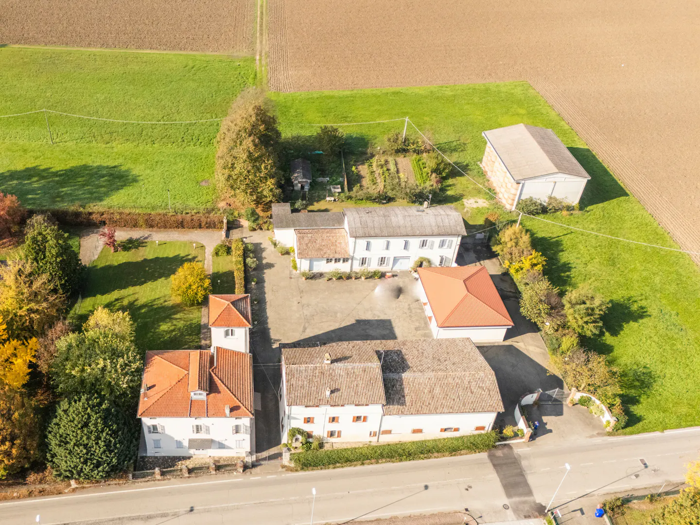 Aerial view of a white house with a red tile roof, surrounded by green fields and trees.