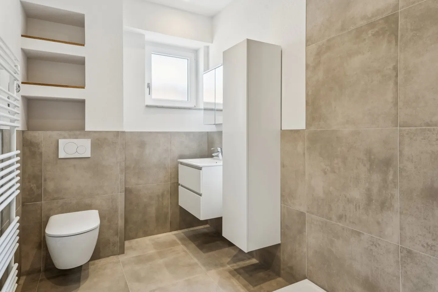 Modern bathroom with beige tiled walls, a wall-mounted white toilet, floating vanity, and built-in recessed shelving.