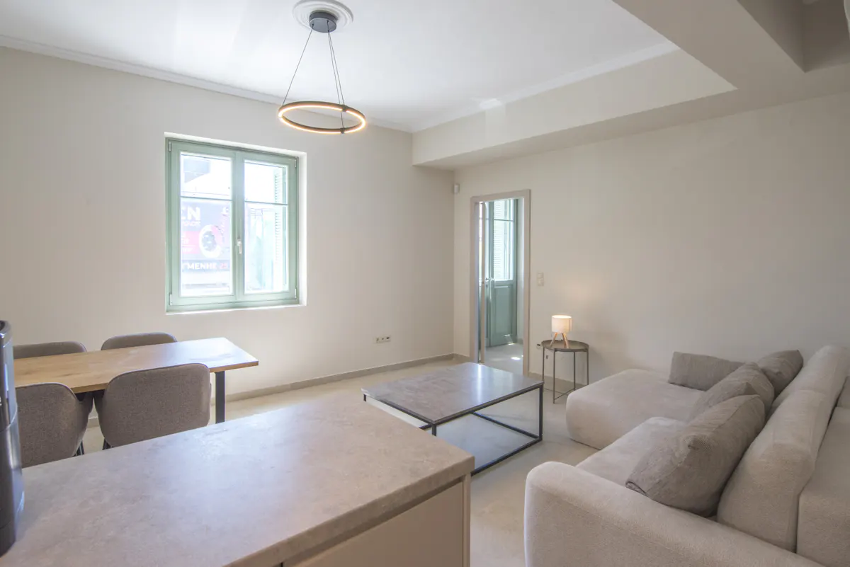 Bright living room with a white sofa, marble coffee table, and a wooden dining table near a green-framed window.