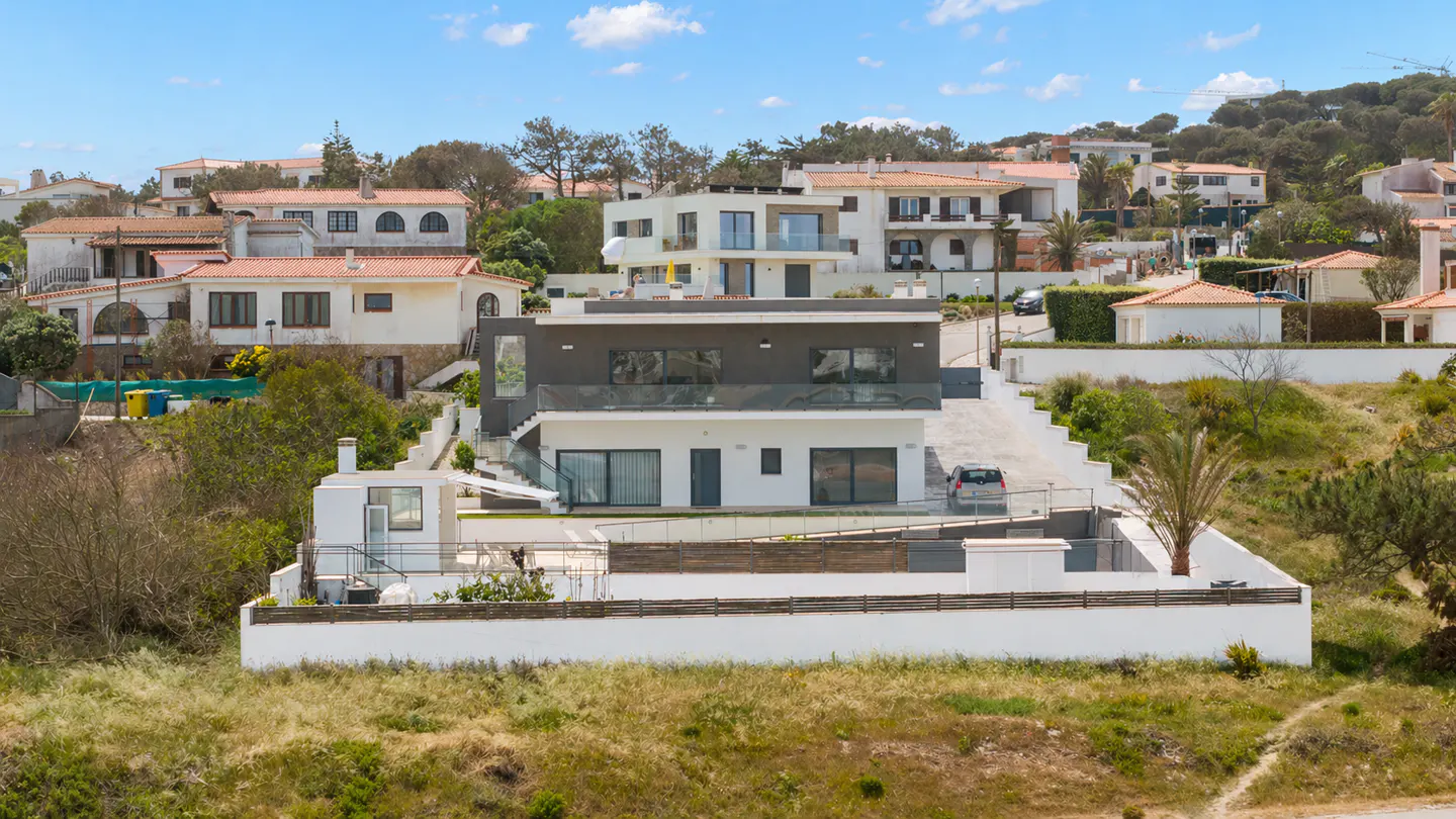 Two-story modern house with gray and white exterior, surrounded by other houses on a sunny day.