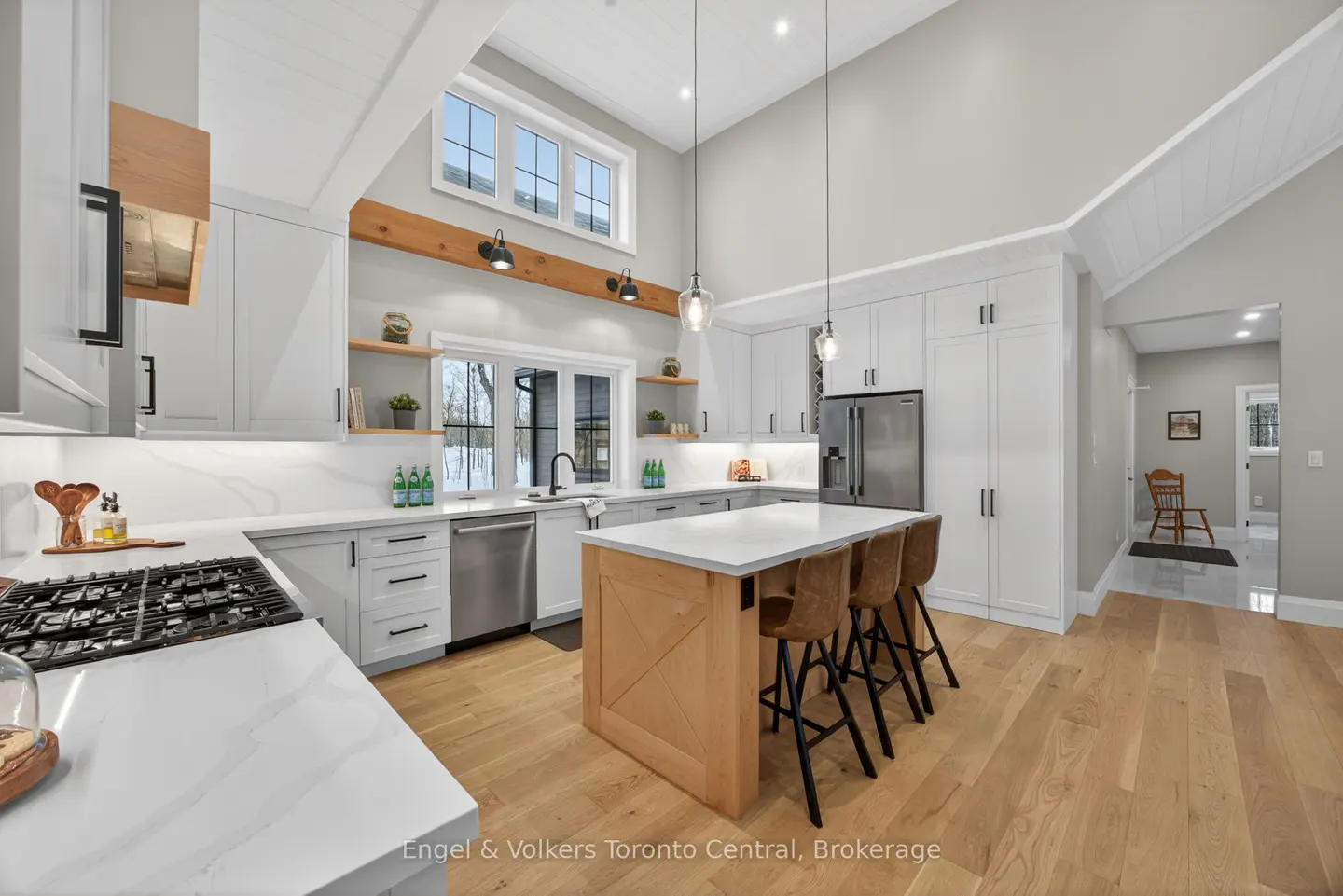 Bright, modern kitchen with white cabinets, wood island with stools, and stainless steel appliances. Hardwood floors and high ceilings.