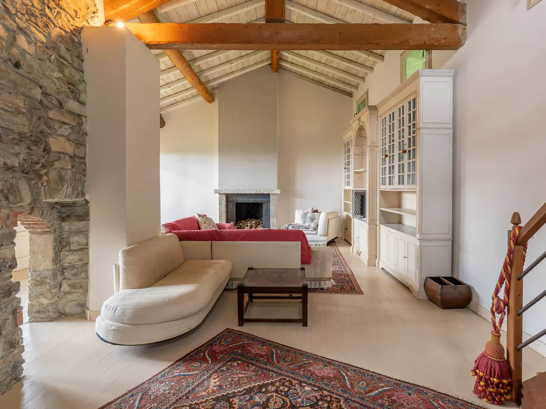 Living room with stone wall, fireplace, and white furniture. A red patterned rug is on the light wood floor.