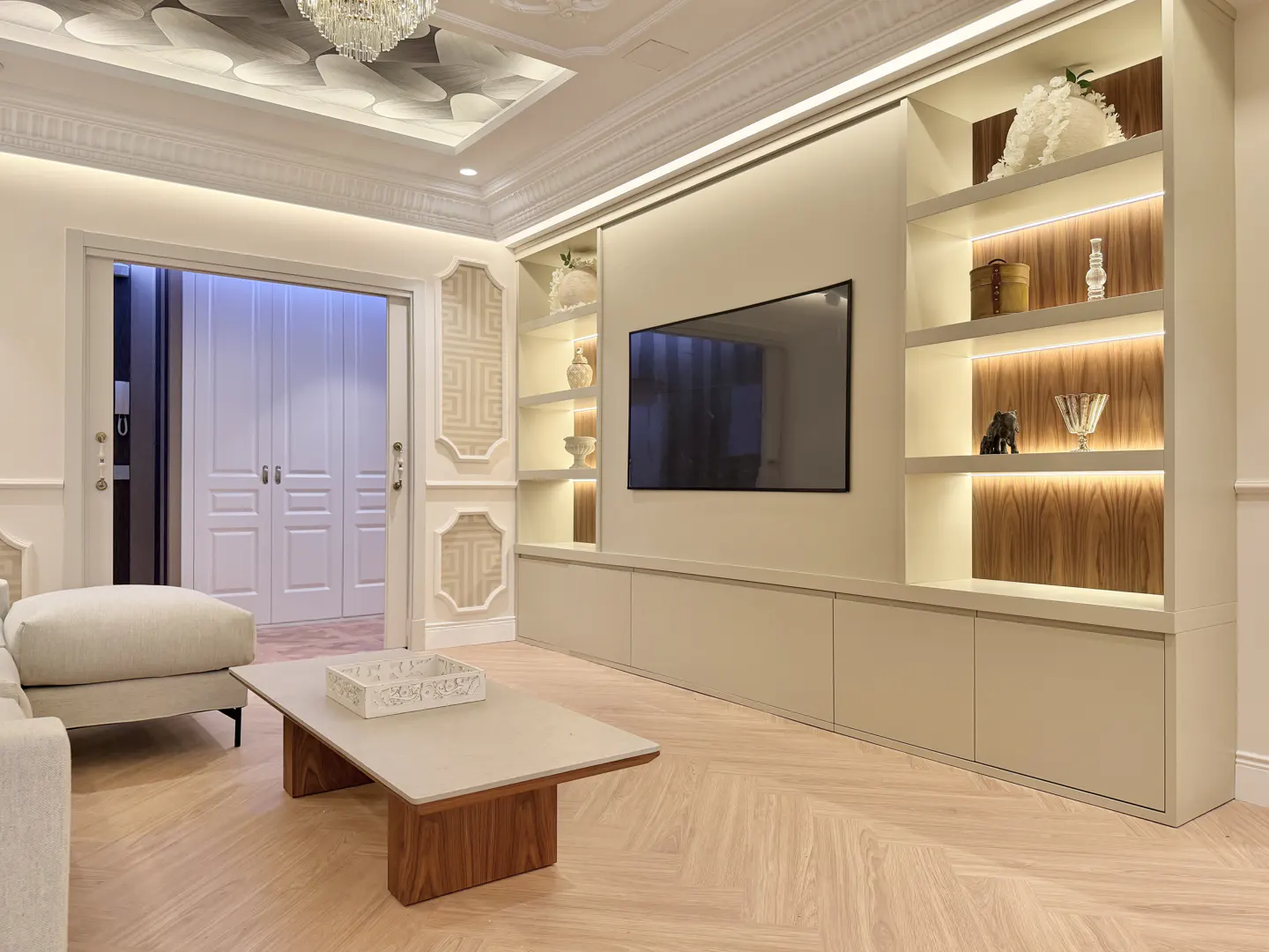 Living room with a TV, built-in shelves with decor, and a light wood coffee table on a herringbone floor.