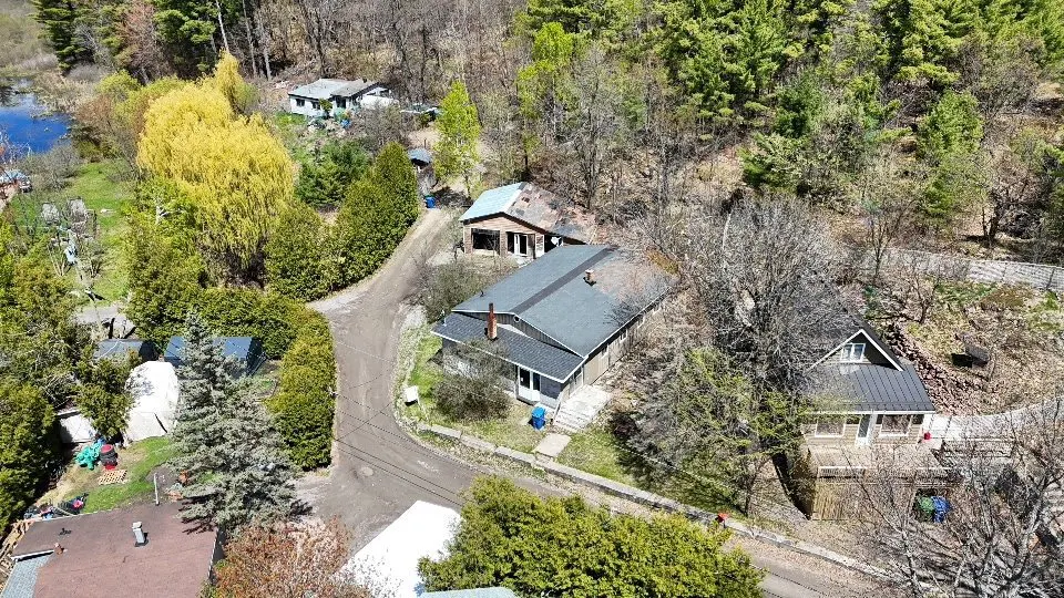 Aerial view of multiple houses nestled among trees, with a dirt road winding through the landscape.