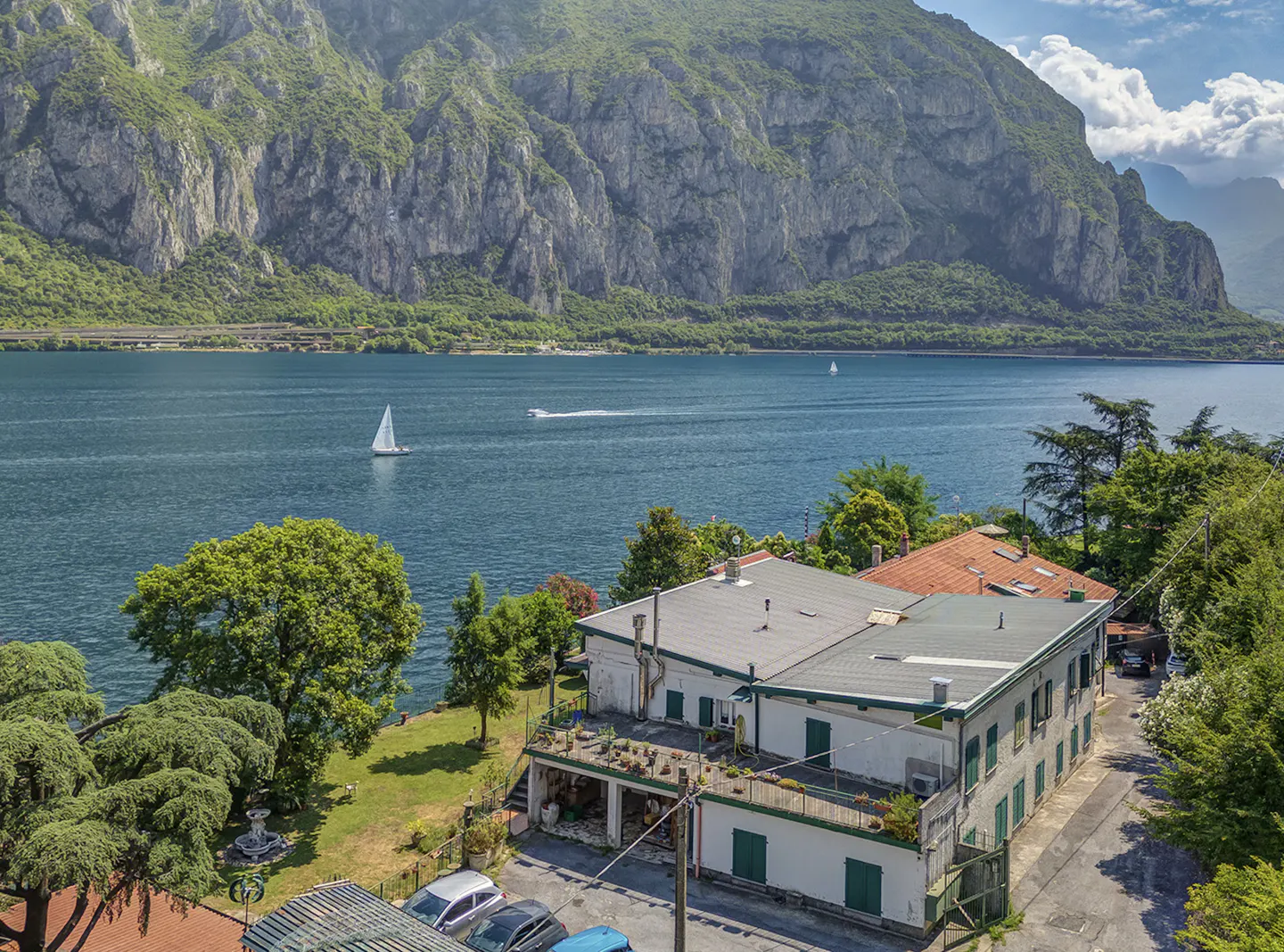 Lake Como view from a white building with green shutters. Mountains, trees, and boats are visible.