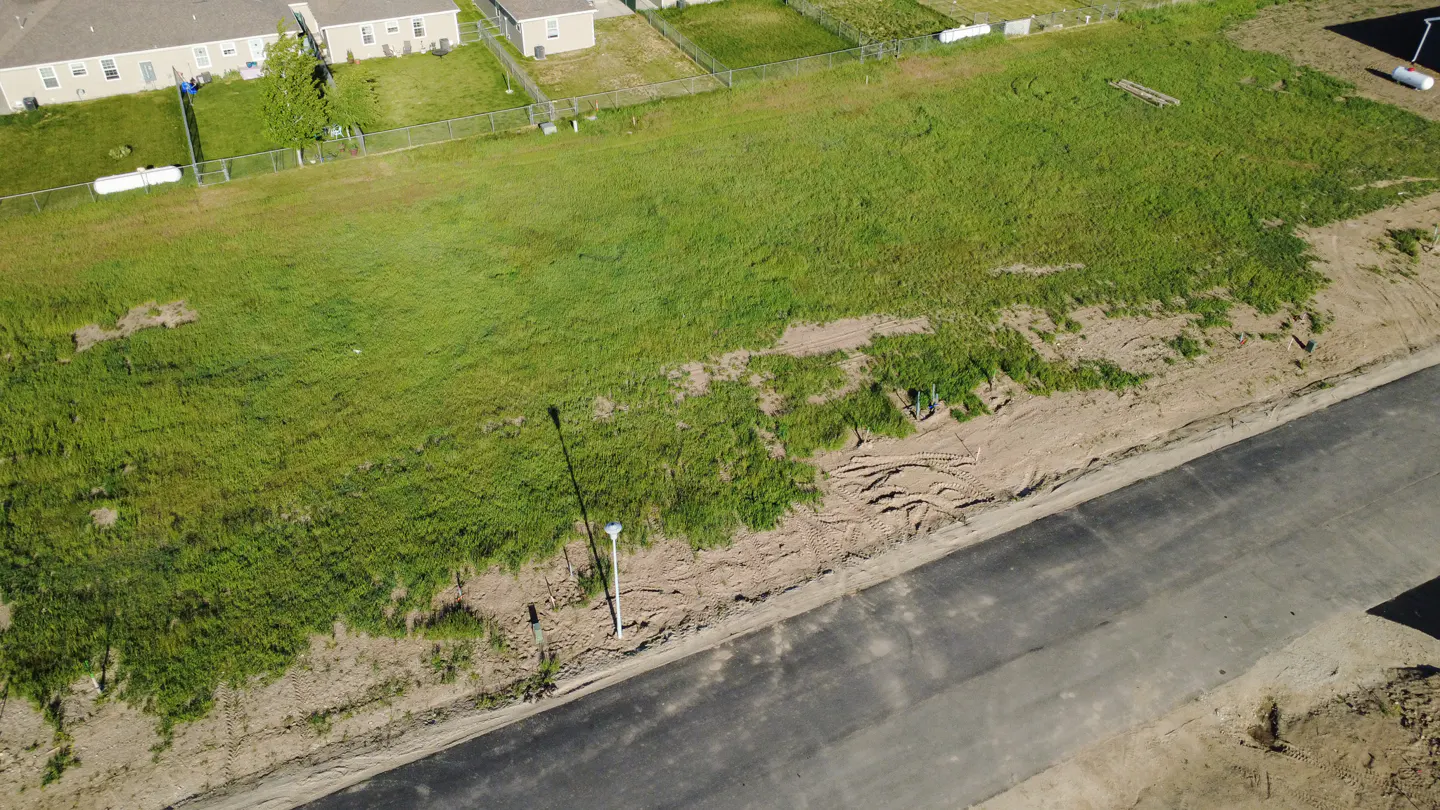 Aerial view of a vacant lot with green grass, a street lamp, and a paved road in a residential area.