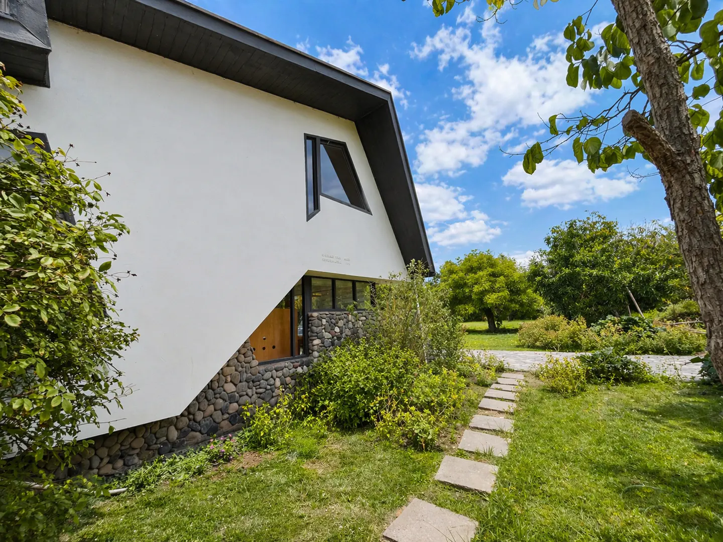 Exterior view of a modern white house with a dark gray roof, stone accents, and a stone pathway leading to the entrance. Blue sky with clouds.