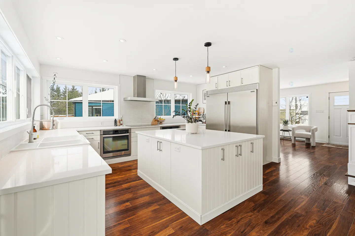Bright, modern kitchen with white cabinets, stainless steel appliances, and a large island with a white countertop on dark wood floors.