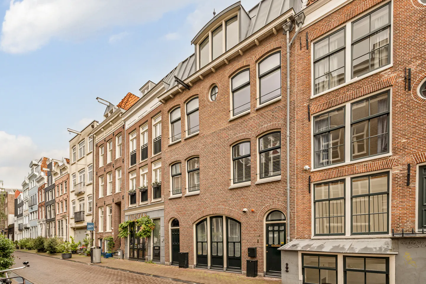 A row of traditional Dutch brick townhouses with large windows and dark frames lining a narrow cobblestone street.