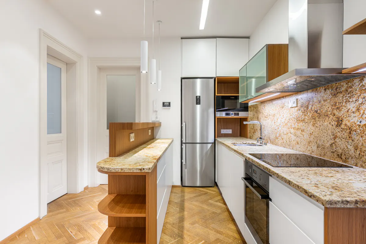 A modern kitchen with white cabinets, stainless steel appliances, and granite countertops. A wooden breakfast bar is on the left.