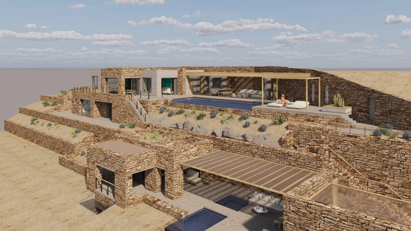 Exterior view of a multi-level stone house with pools, patios, and desert landscaping under a cloudy sky.