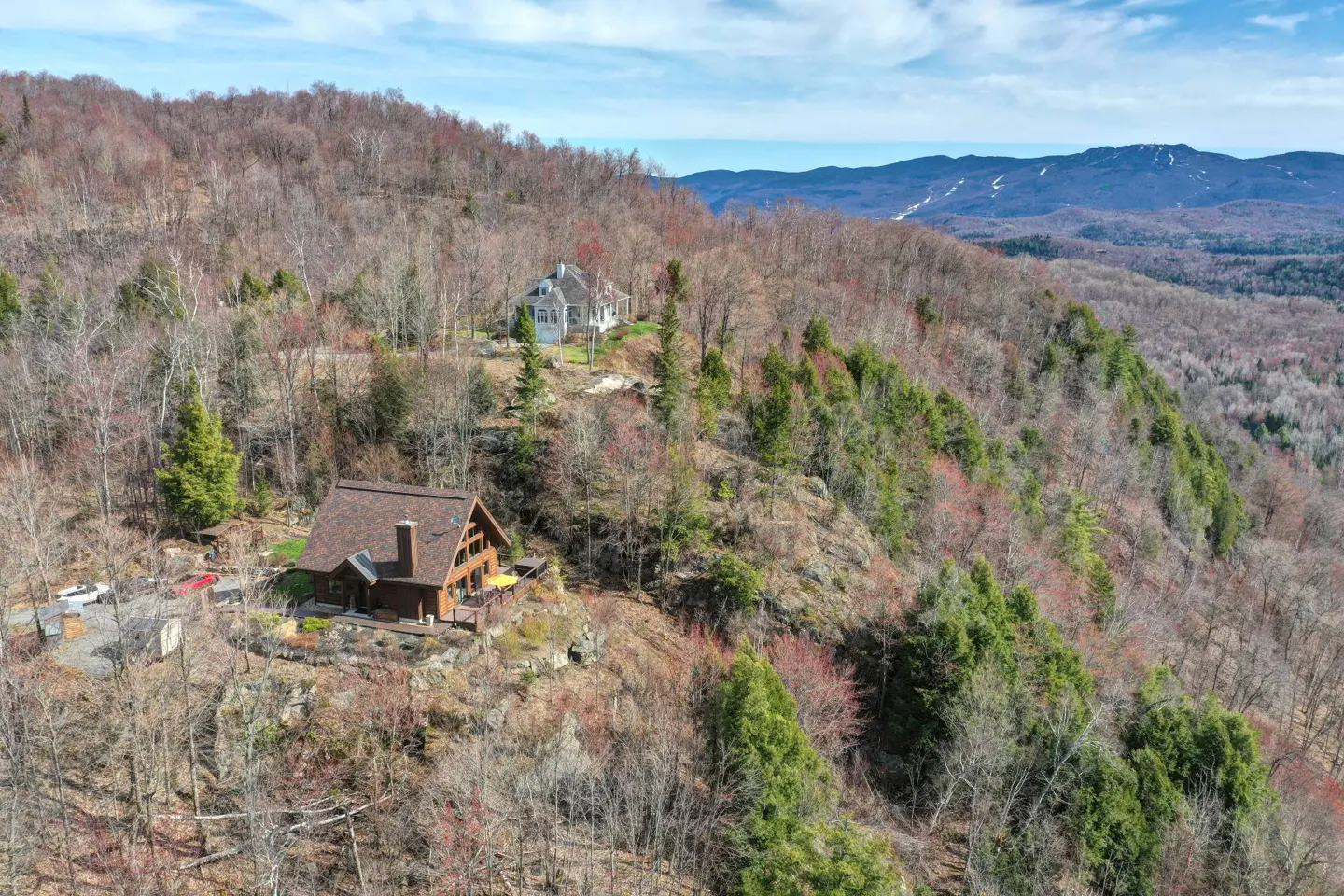 A landscape view of two houses on a wooded hillside with mountains in the background.