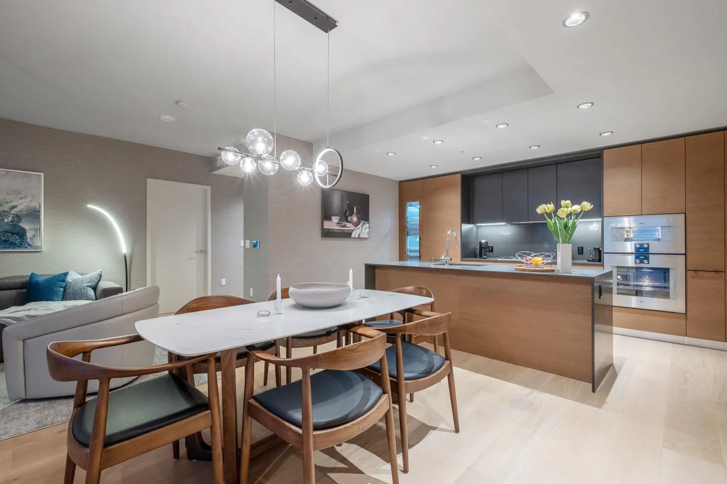 A modern condo interior with a dining table, chairs, and a kitchen island. The color palette is neutral with wood accents.