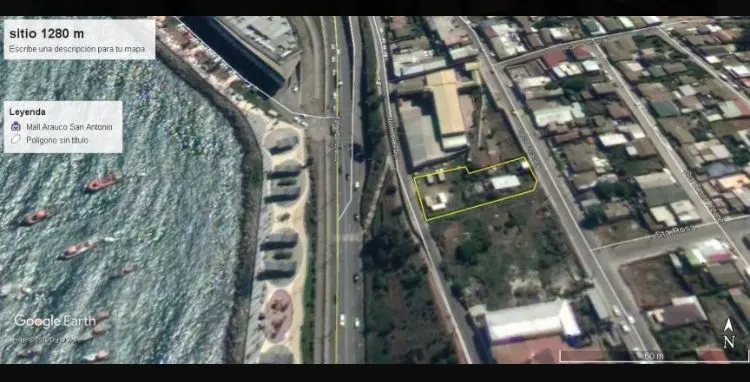 Aerial view of a property outlined in yellow, near a highway and the ocean, with buildings and houses nearby.