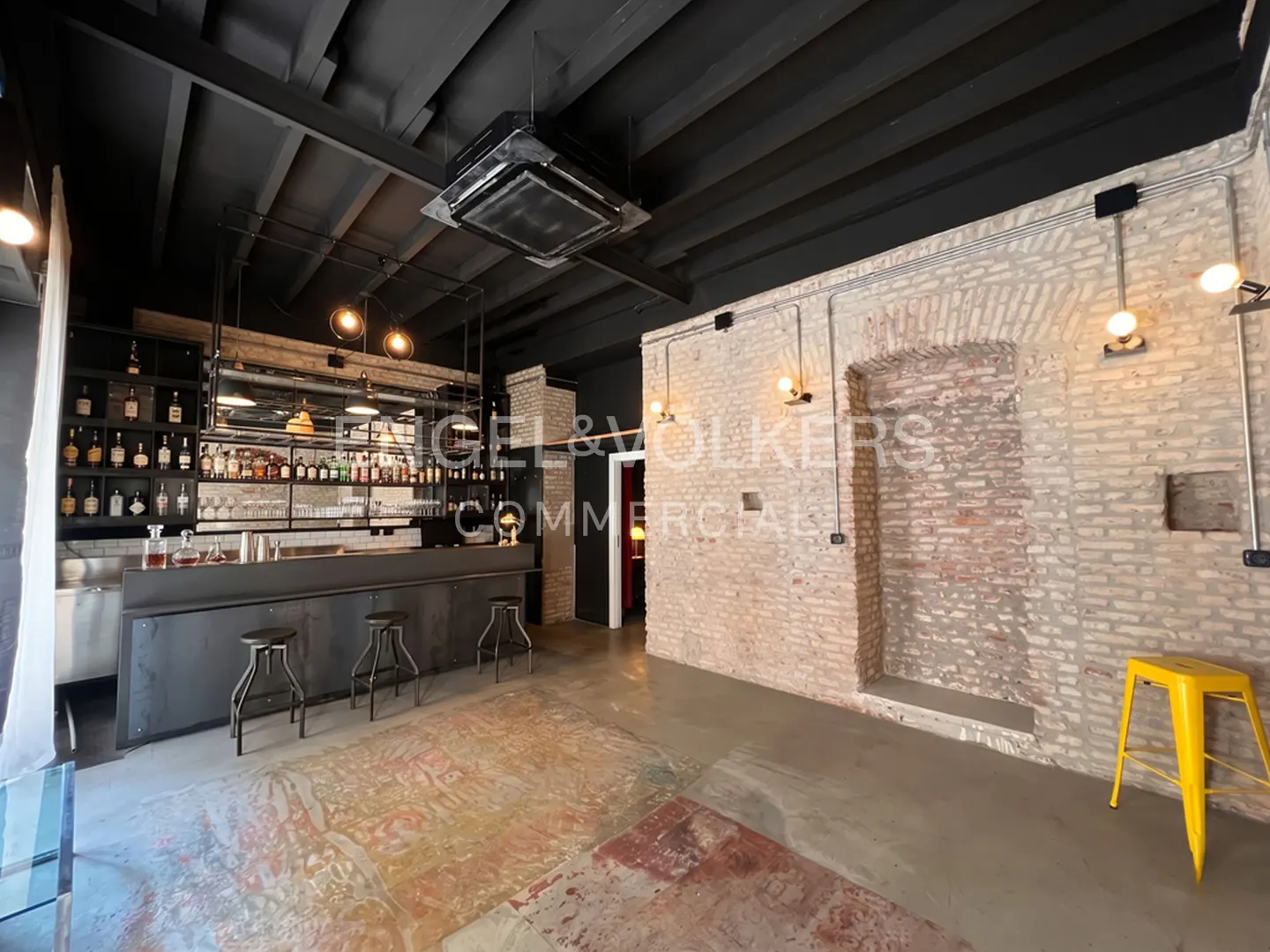 Interior view of a commercial space with a bar, brick walls, and a yellow stool.