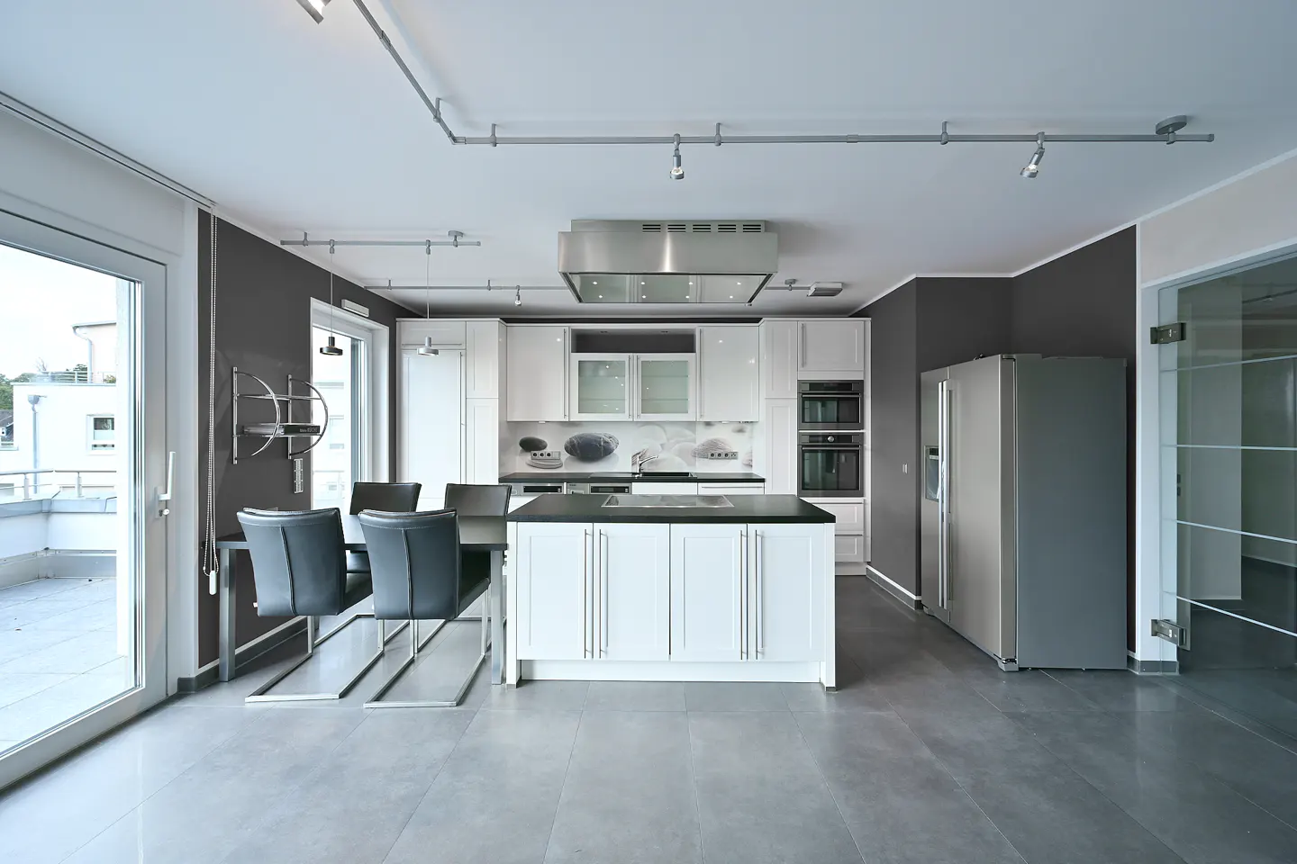 A modern kitchen with white cabinets, a black countertop island, stainless steel appliances, and a dining table with gray chairs.