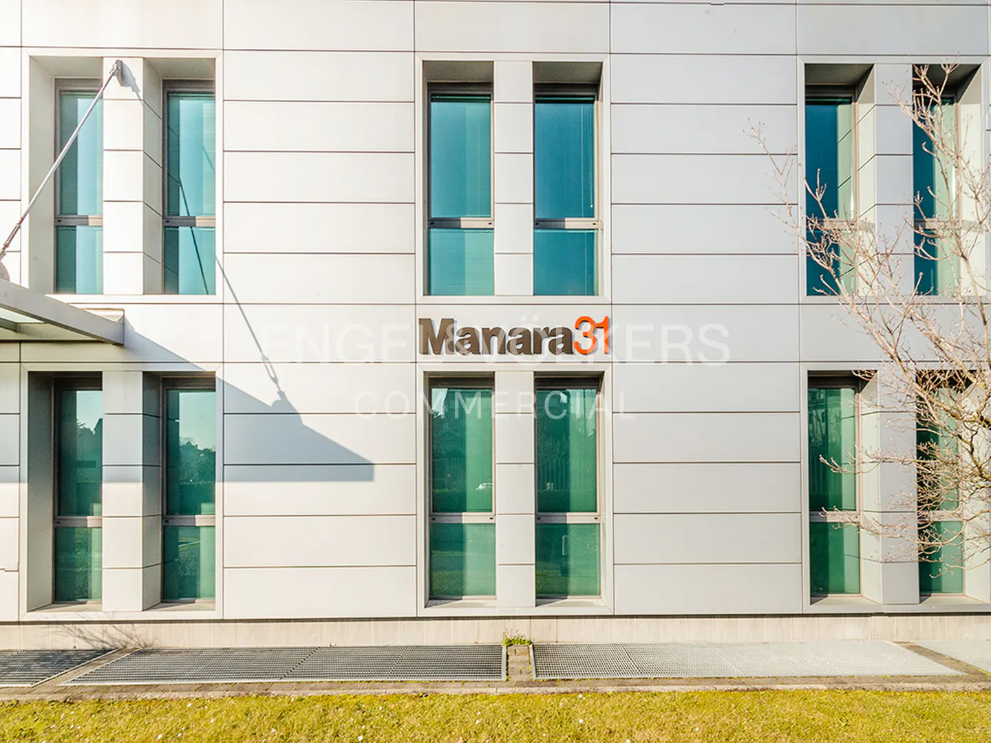Modern office building facade with white panels, symmetrical windows, and the sign "Manara 31" centered on the wall.